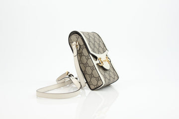Gucci Horsebit 1955 monogram canvas phone bag in beige and white leather with adjustable strap and gold accents.