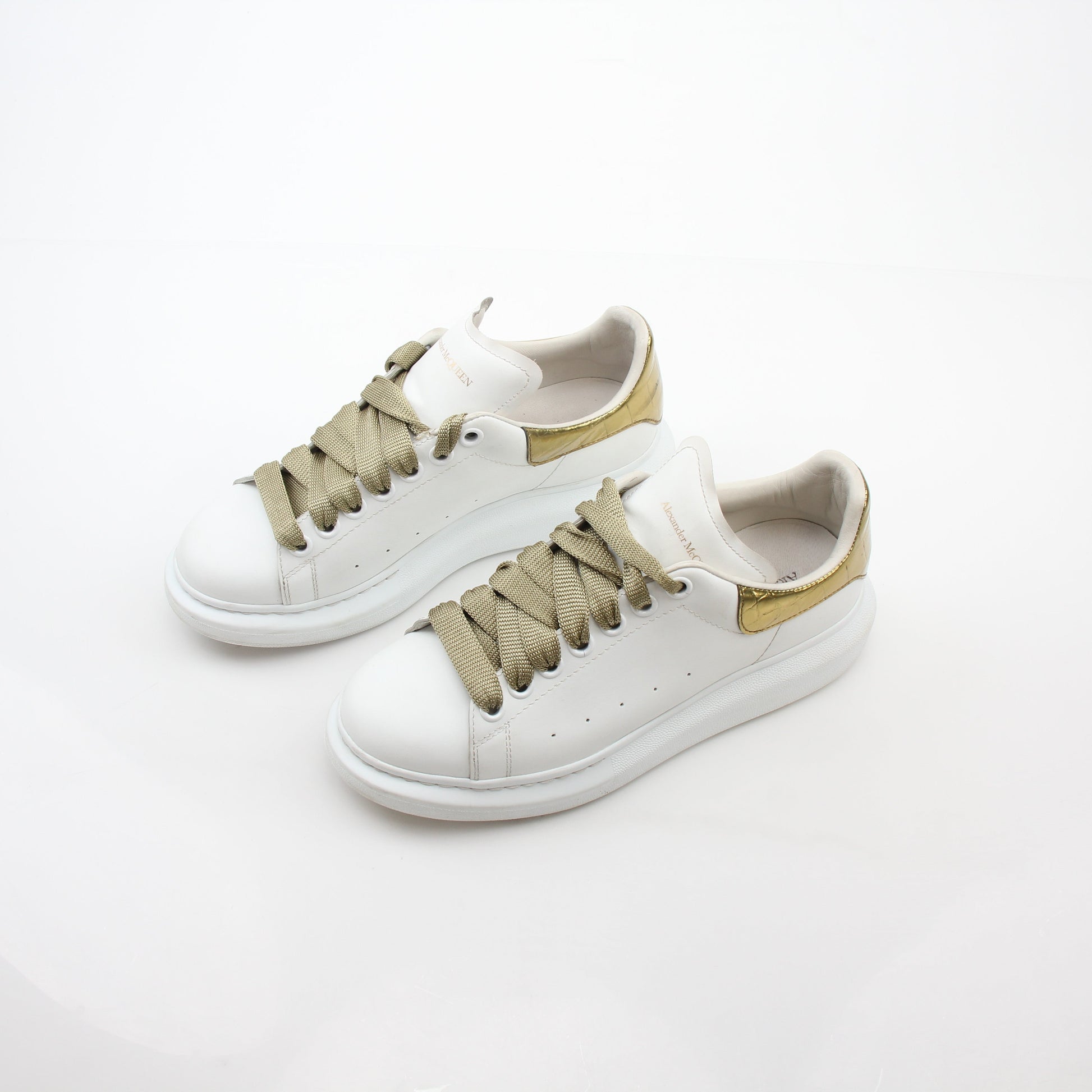 Alexander McQueen white gold oversized low-top sneakers with chunky design and laces, displayed on a plain background.