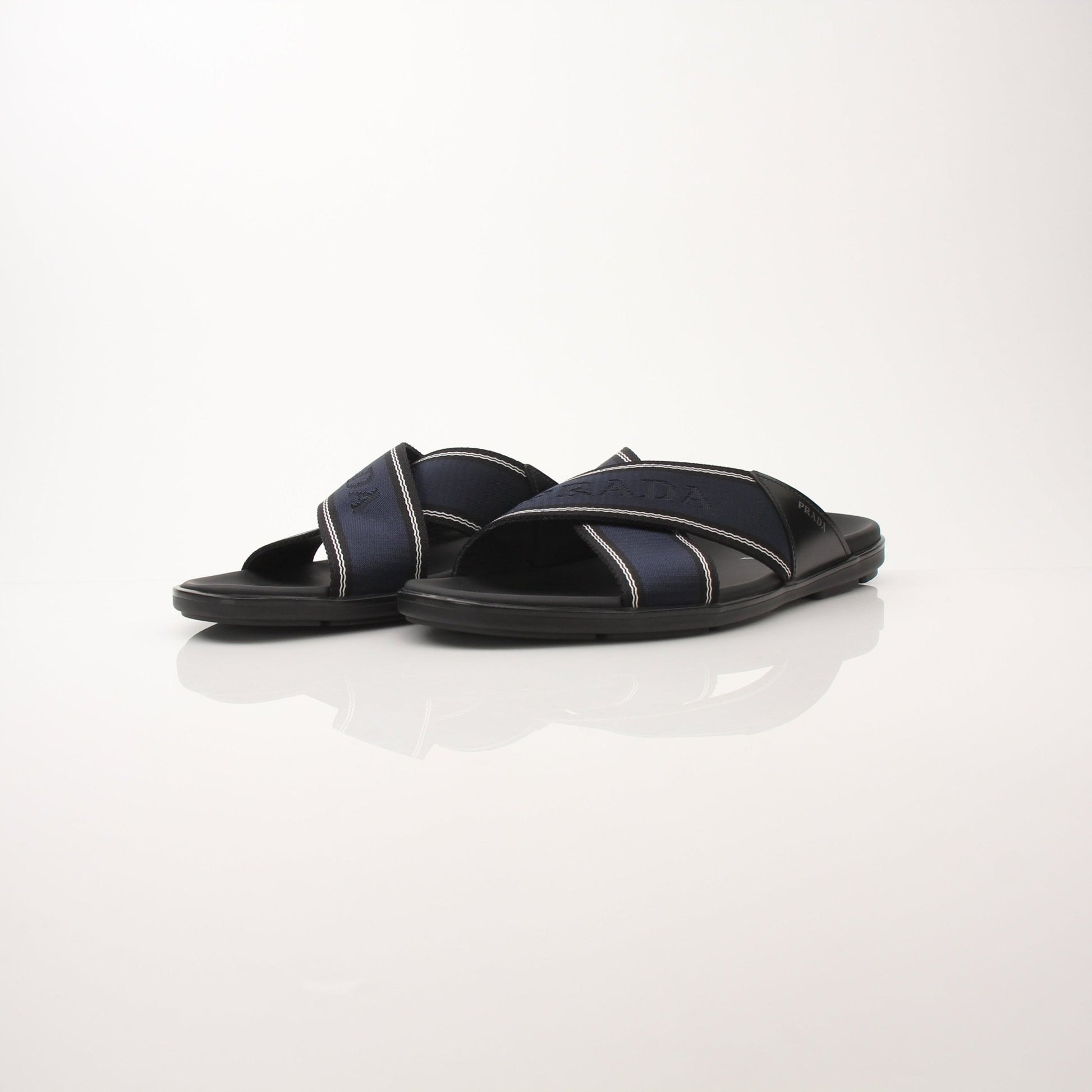 Prada men's leather and Re-Nylon sandals, black and beige, with open toe and strap design, displayed on a neutral background.