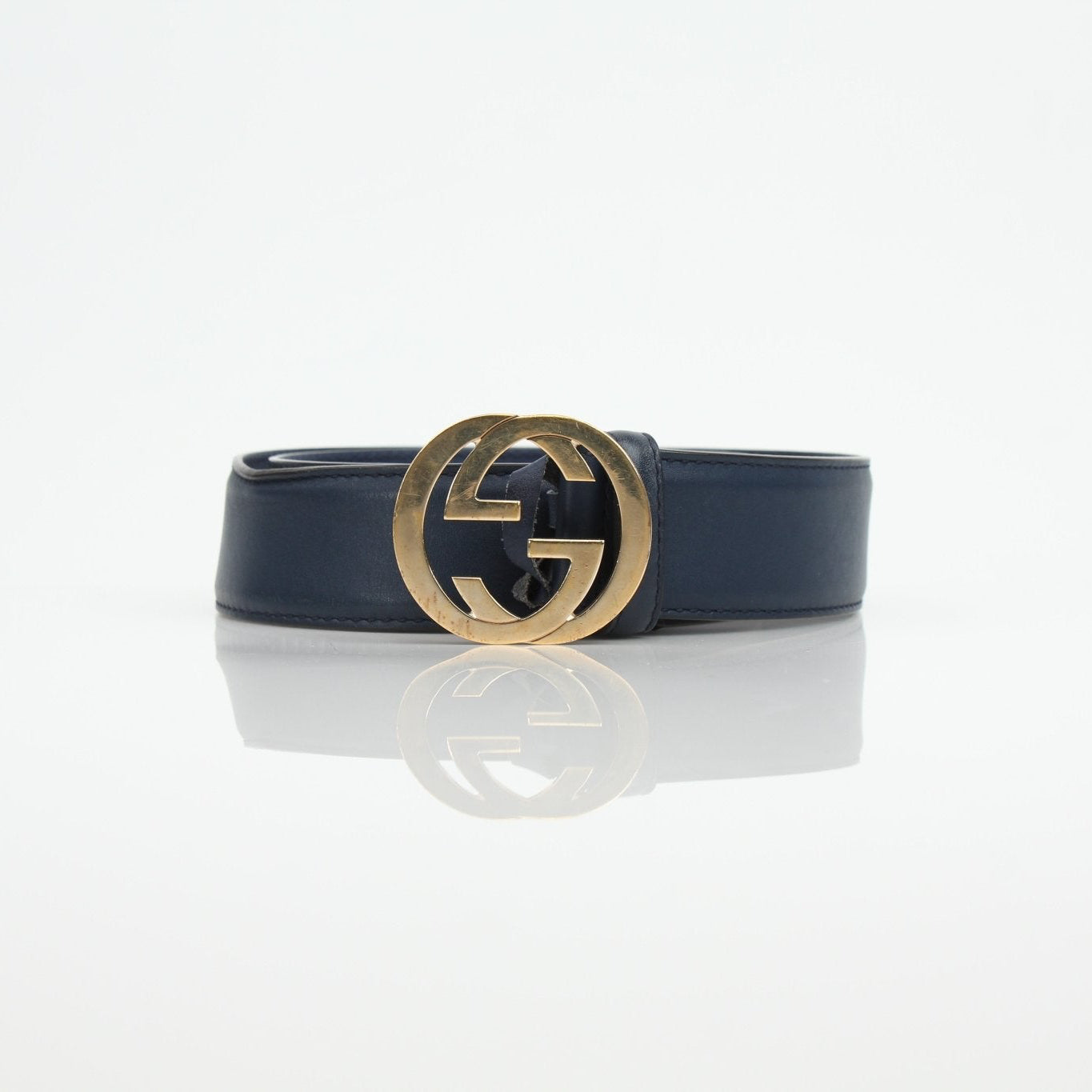 Gucci navy interlocking GG belt with gold hardware, stylish accessory for men and women, displayed on a neutral background.