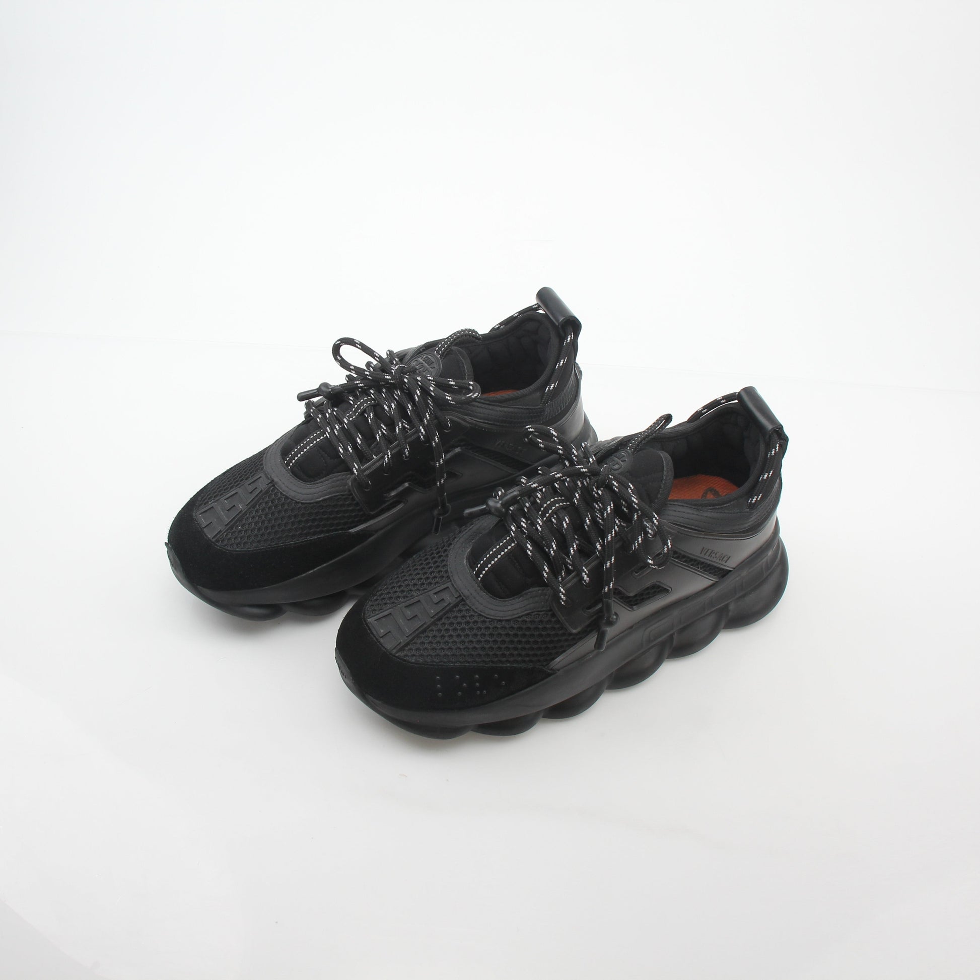 Black Chain Reaction sneakers by Versace with gold accents, featuring a sleek design and bold chain details, displayed on a white background.