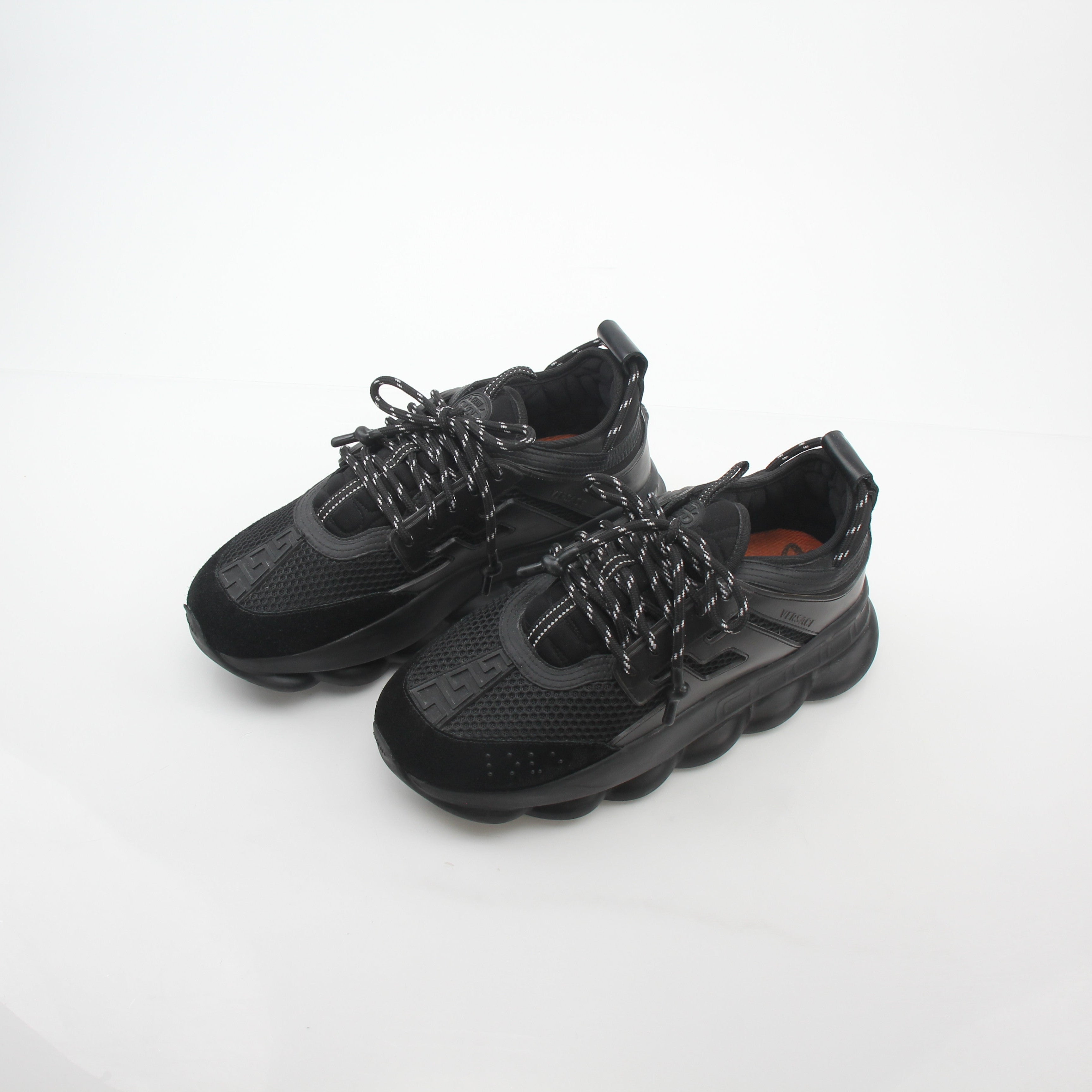 Black Chain Reaction sneakers by Versace with gold accents, featuring a sleek design and bold chain details, displayed on a white background.