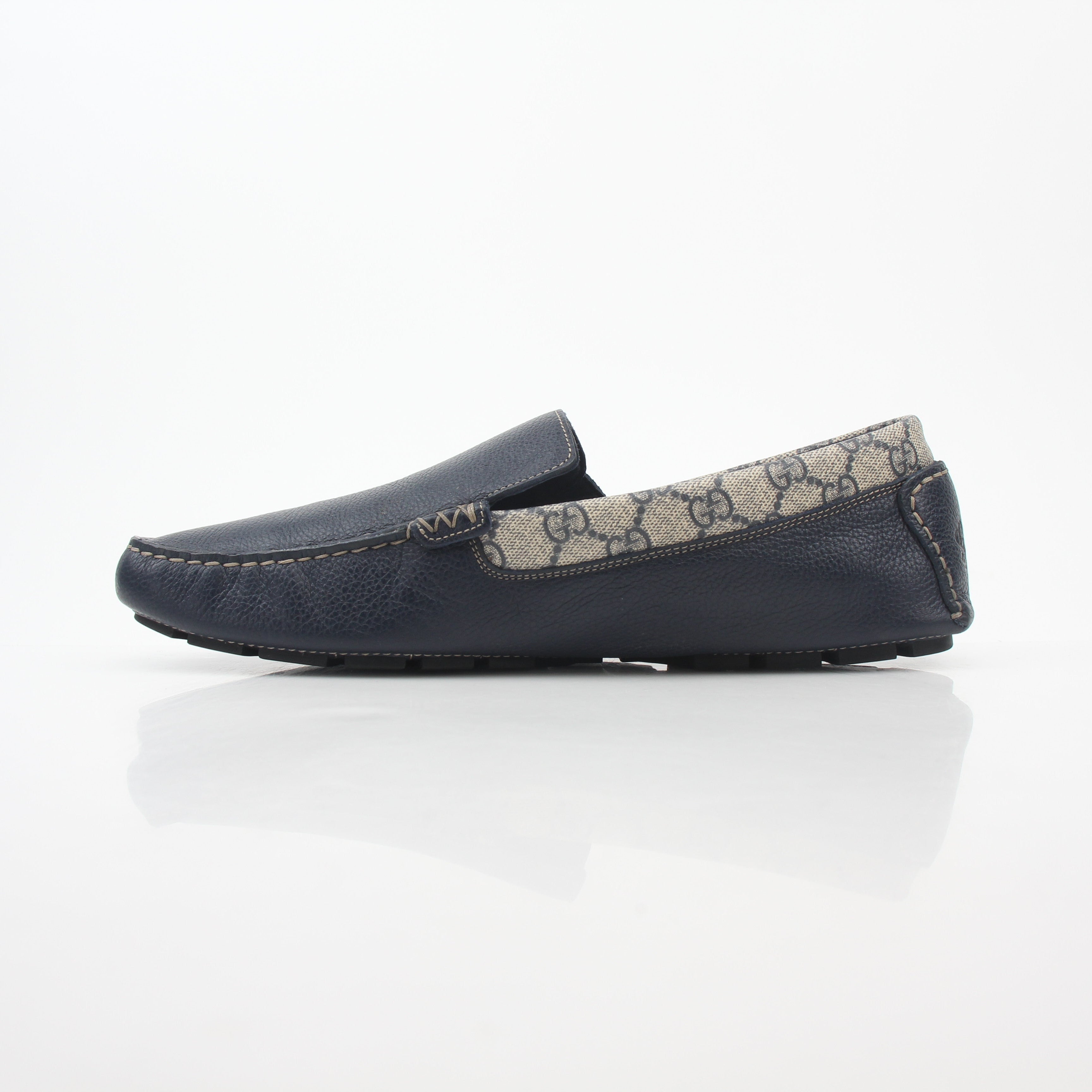 Gucci navy GG Supreme leather driver loafers with gold accents, stylish men's shoes on a neutral background.
