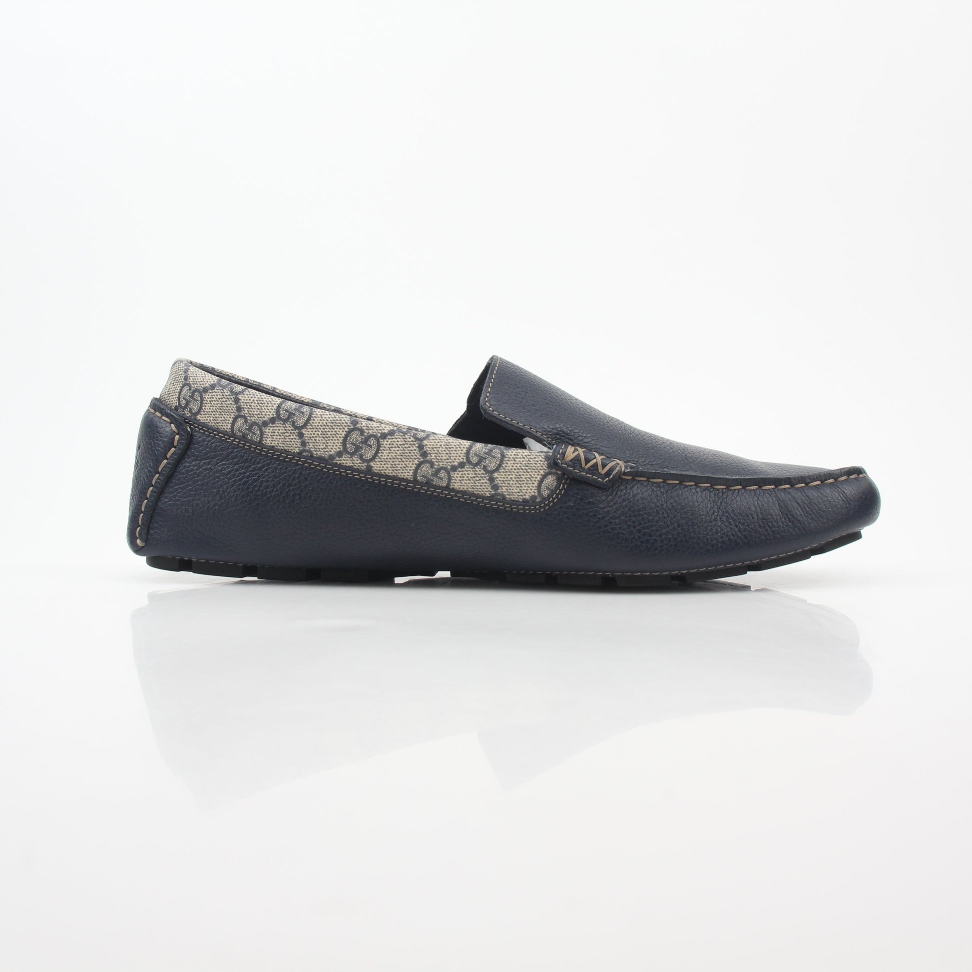 Gucci navy GG Supreme leather driver loafers with classic slip-on design and gold accents, displayed on a neutral background.