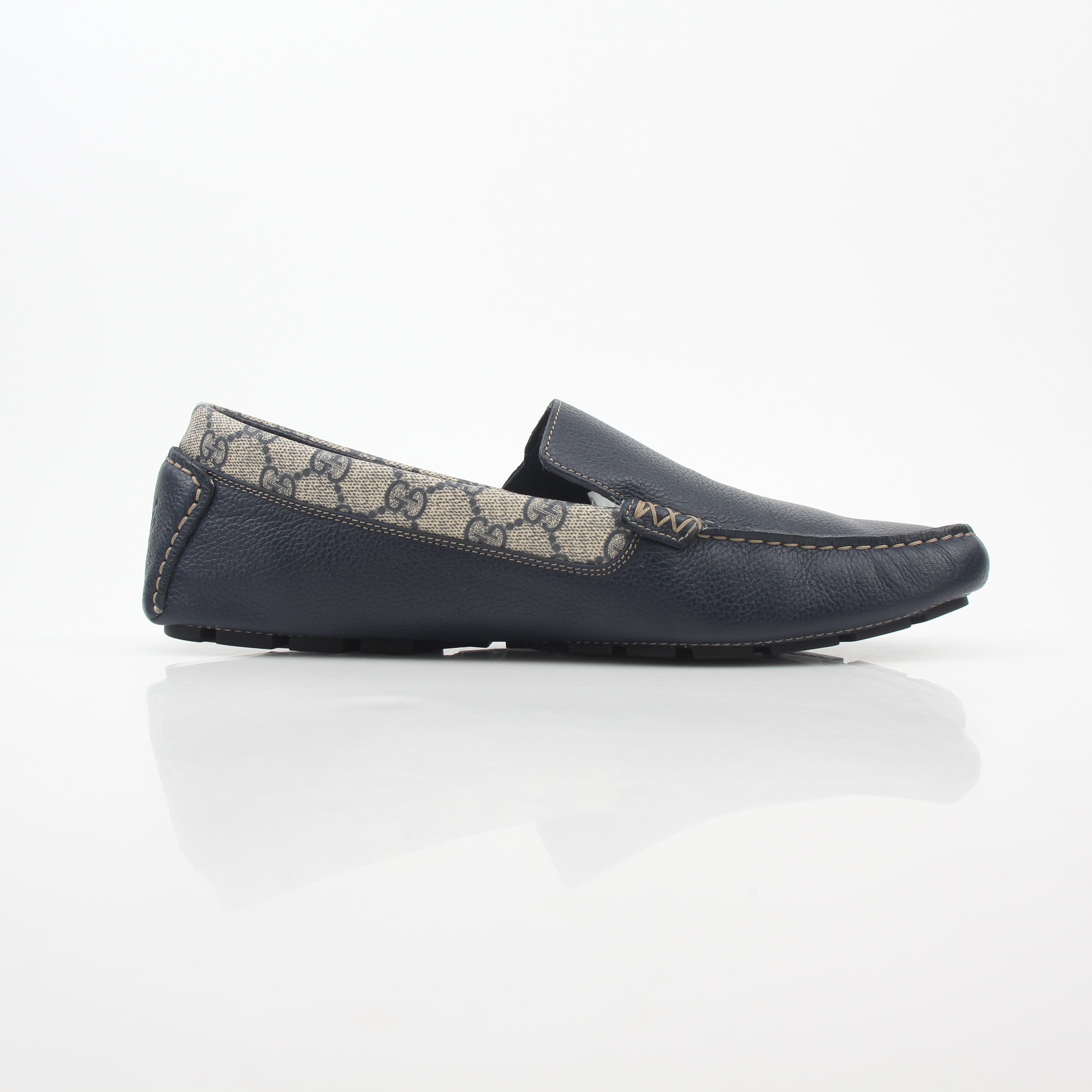 Gucci navy GG Supreme leather driver loafers with classic slip-on design and gold accents, displayed on a neutral background.