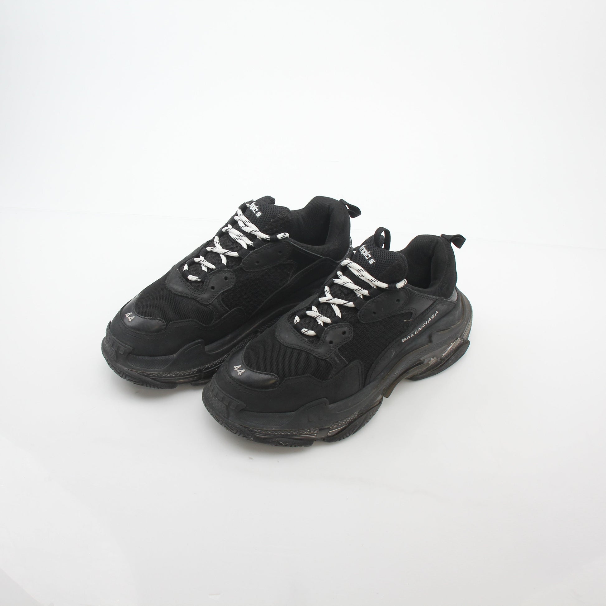 Black Balenciaga Triple S sneakers with clear soles, featuring chunky design and black laces, on a plain background.