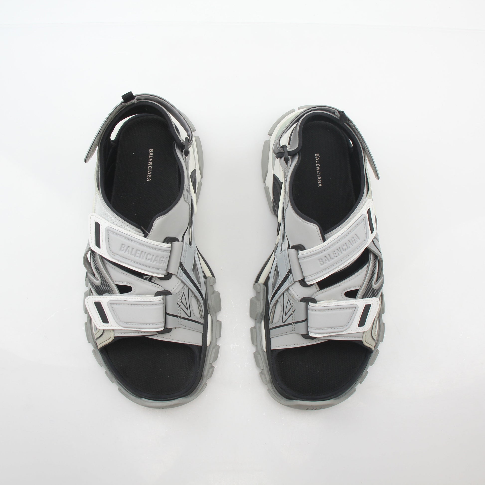 Grey Balenciaga track sandals with sporty design, featuring chunky soles and adjustable straps, worn by a person in casual attire.