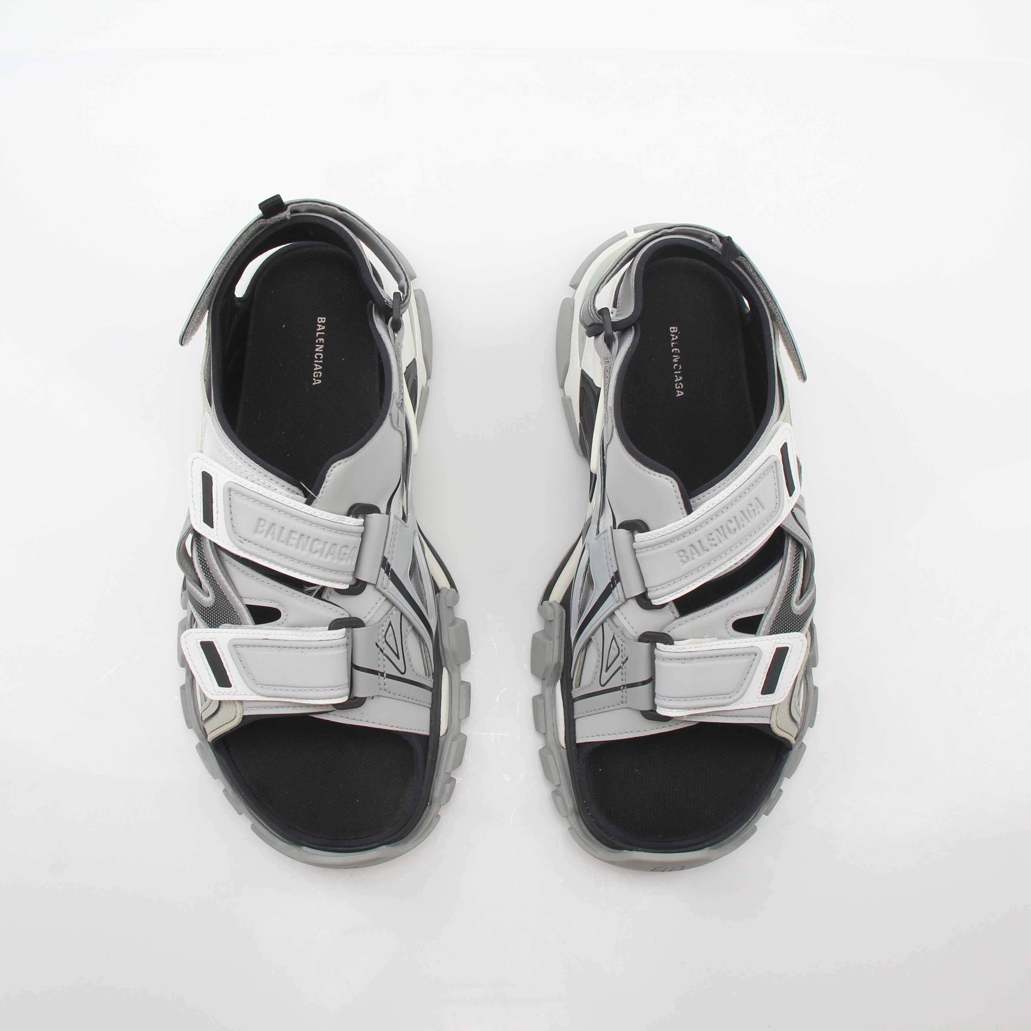 Grey Balenciaga track sandals with sporty design, featuring chunky soles and adjustable straps, worn by a person in casual attire.