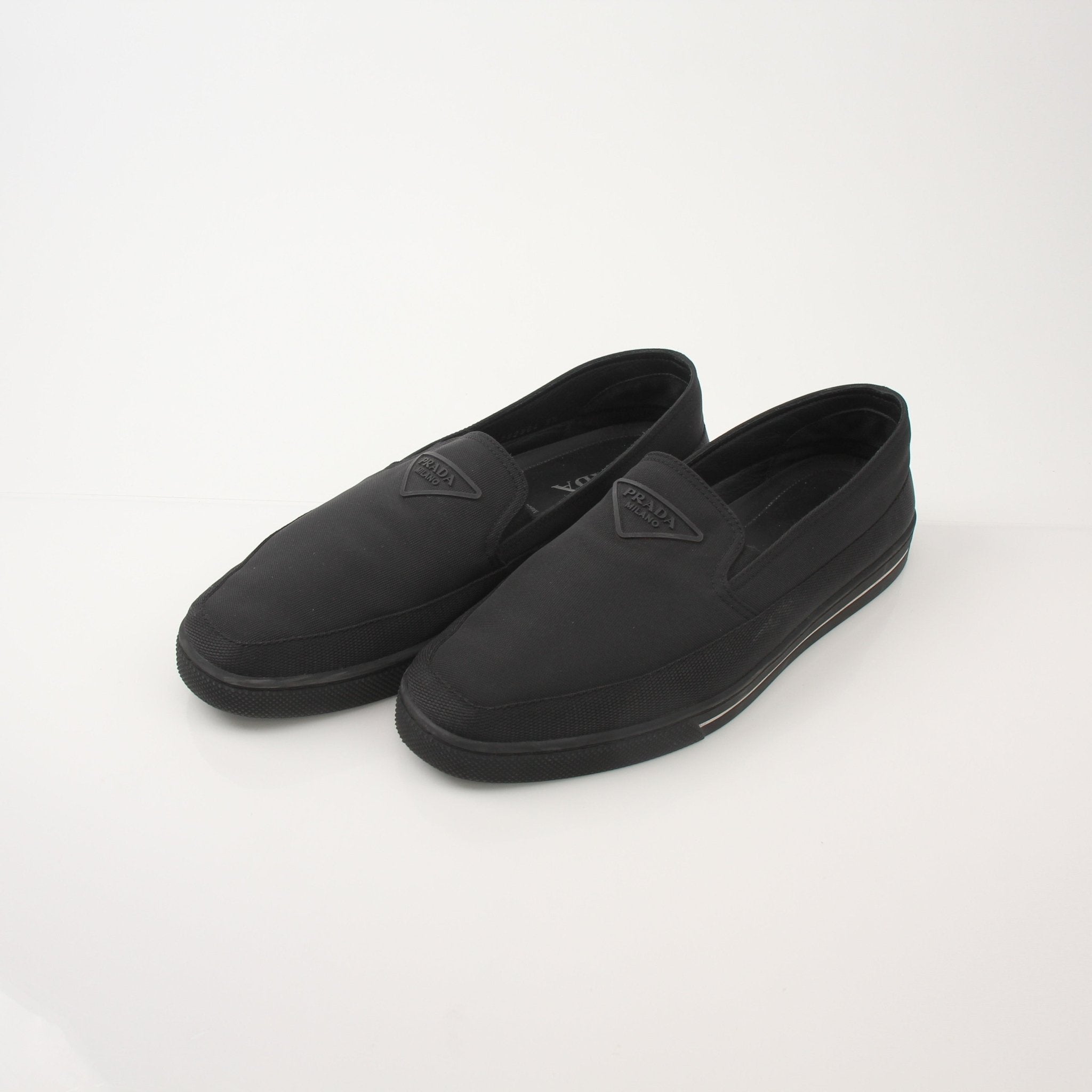 Prada men's triangle logo nylon slip-on loafers with sleek design and durable nylon material, featuring classic slip-on style and brand emblem.