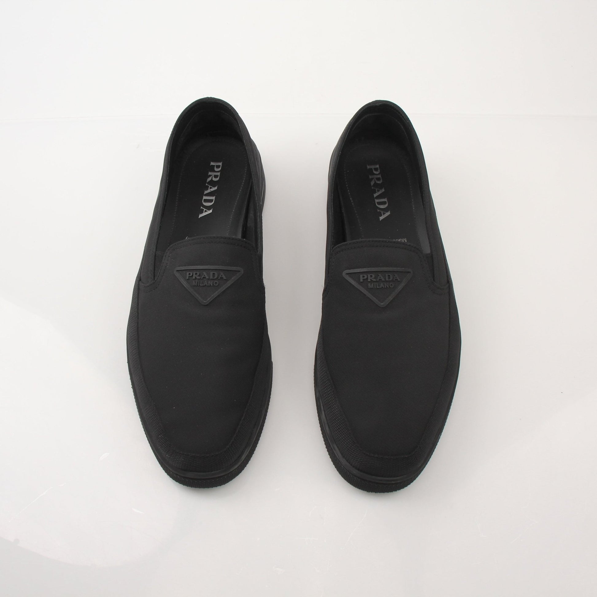 Prada men's triangle logo nylon slip-on loafers with black soles and sleek design, showcasing the iconic logo on the upper.