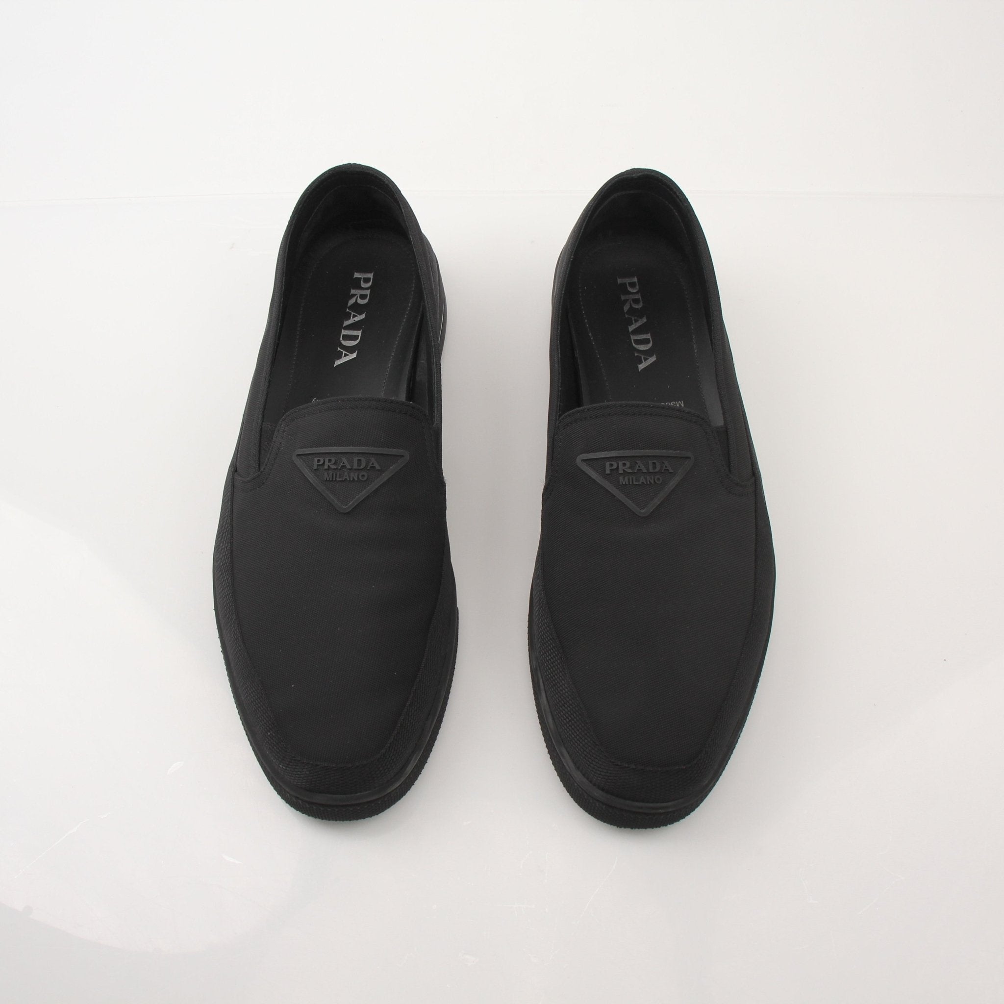 Prada men's triangle logo nylon slip-on loafers with black soles and sleek design, showcasing the iconic logo on the upper.