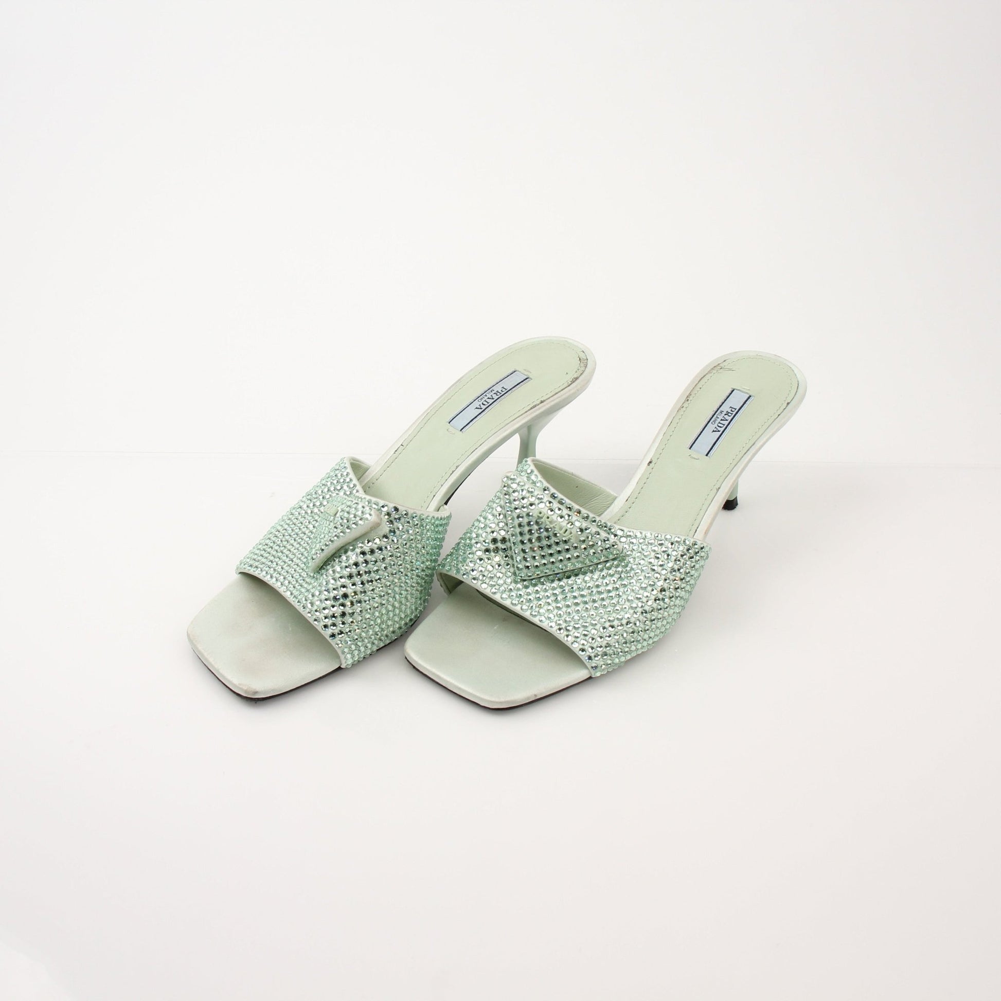 Prada women's crystal-embellished open-toe mules featuring elegant heels with sparkling crystal details and stylish design.