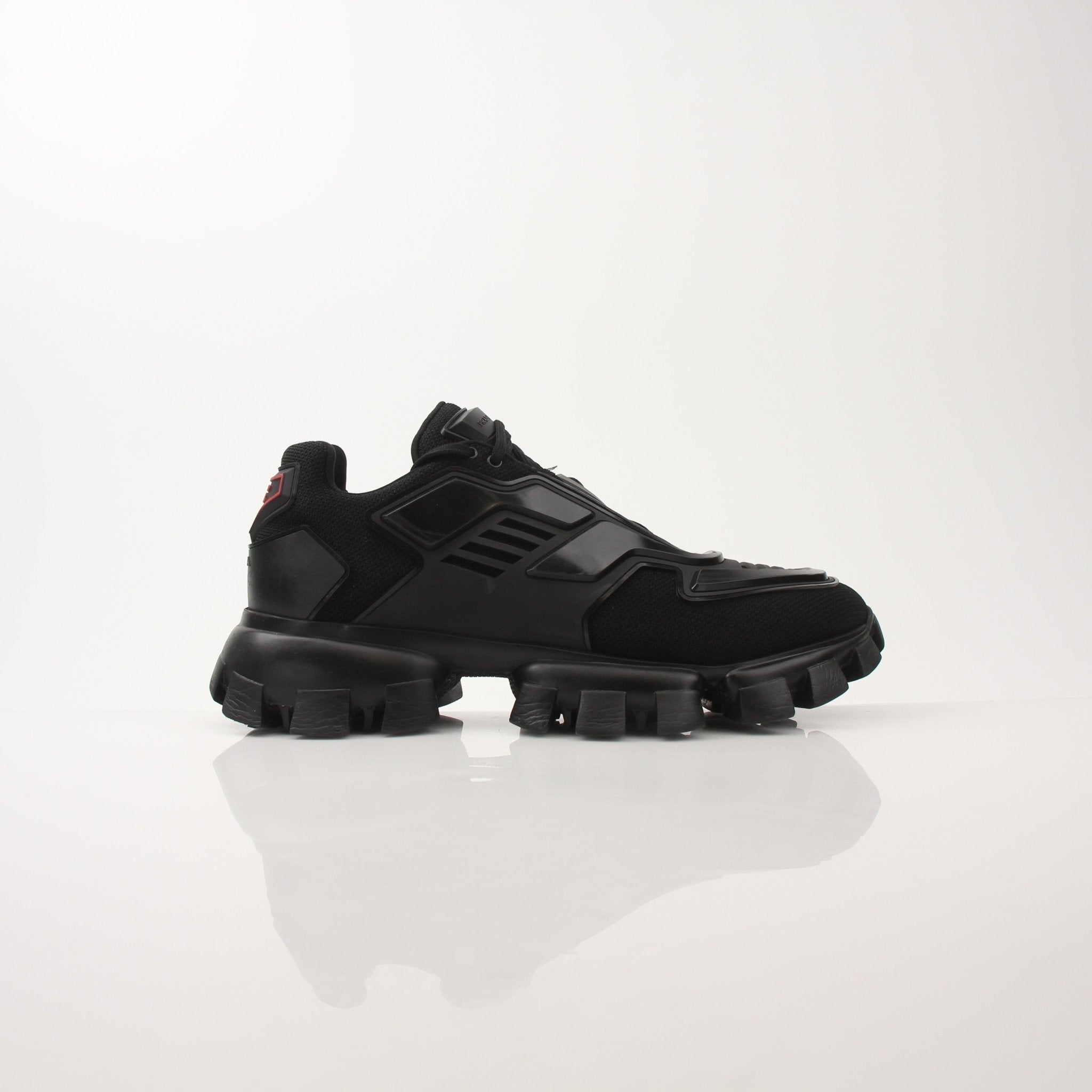 Prada Men’s Cloudbust Thunder knit fabric sneakers in black and white with gold accents, showing the shoe's side profile and laces.