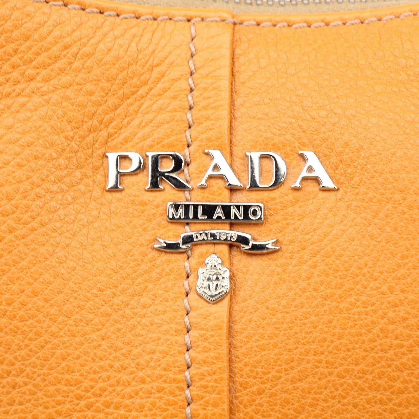Prada orange Daino leather handbag with sleek design and top handle, featuring elegant stitching and polished hardware.