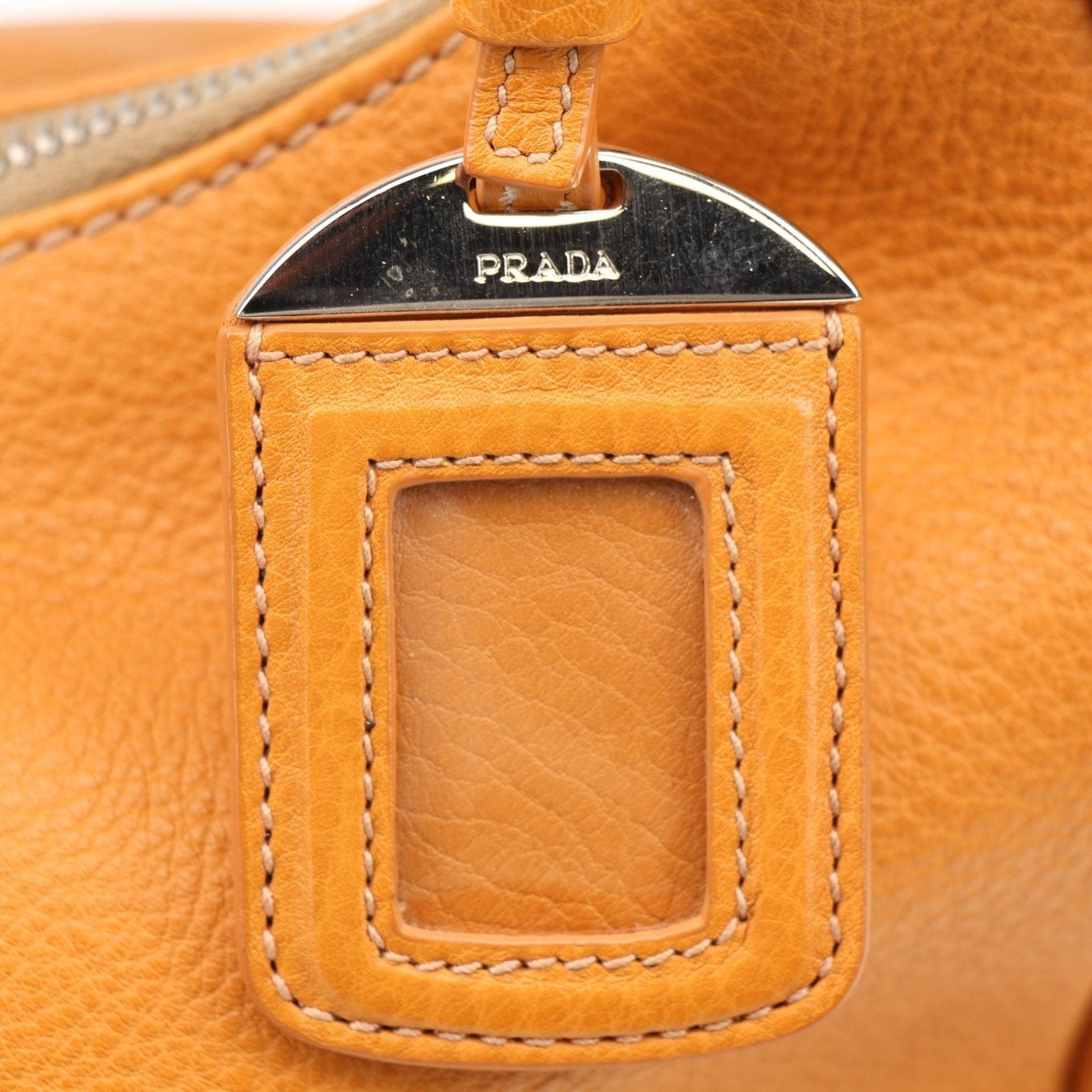 Prada orange Daino leather handbag with top handles and sleek design, showcasing luxurious craftsmanship and vibrant color.