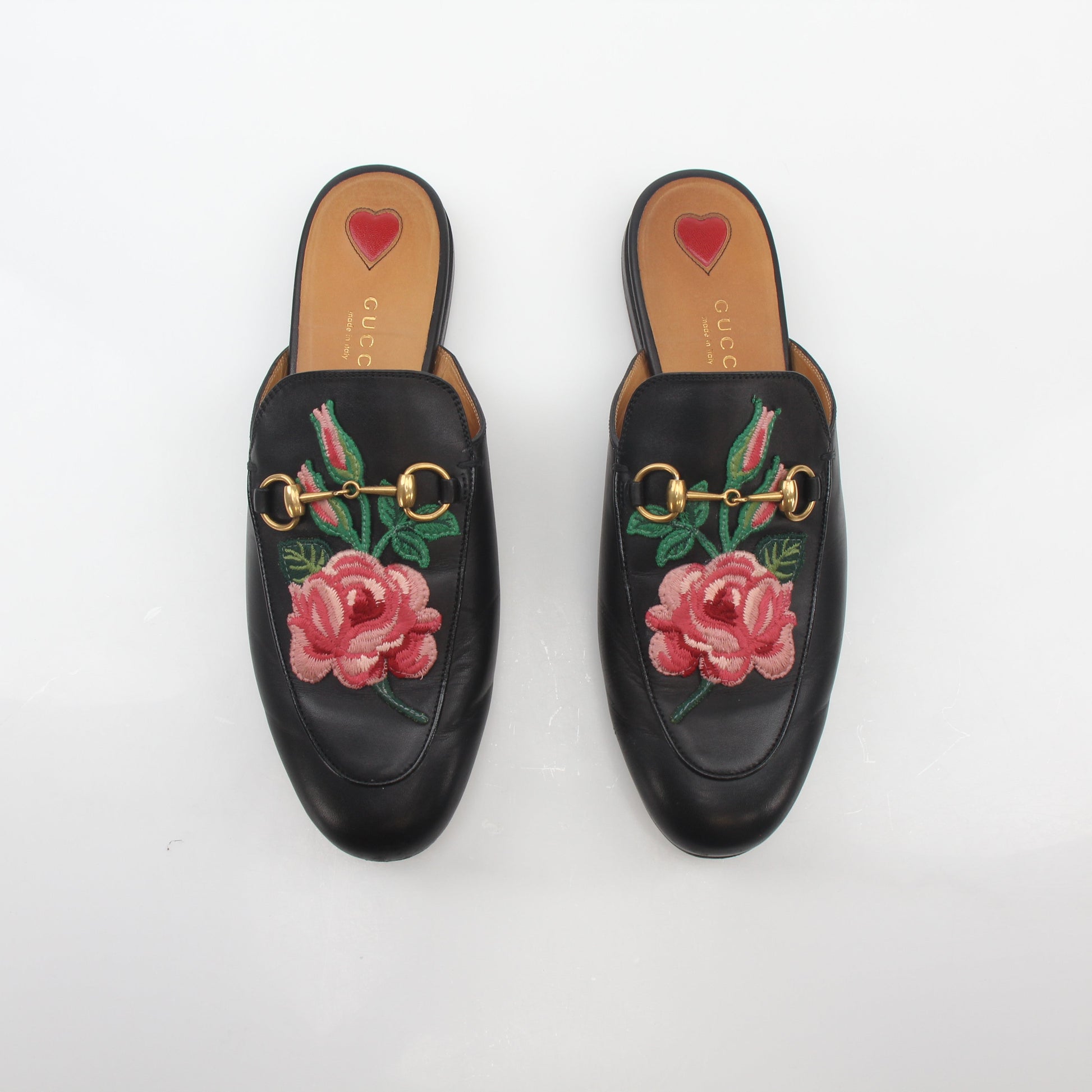 Black Gucci Princetown leather mules with rose embroidery, showcasing a stylish slip-on shoe with a pointed toe and textured leather finish.