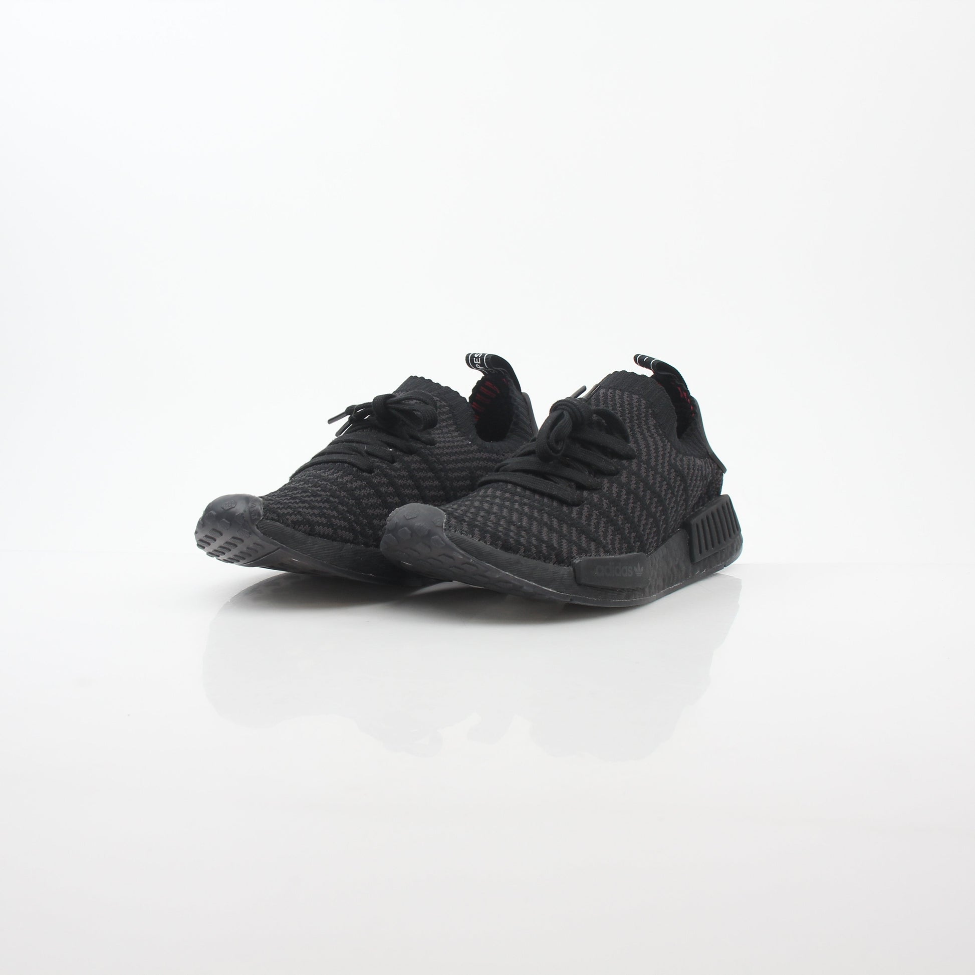Black Adidas NMD R1 STLT Primeknit sneakers with Boost sole and white accents, displayed on a plain background.
