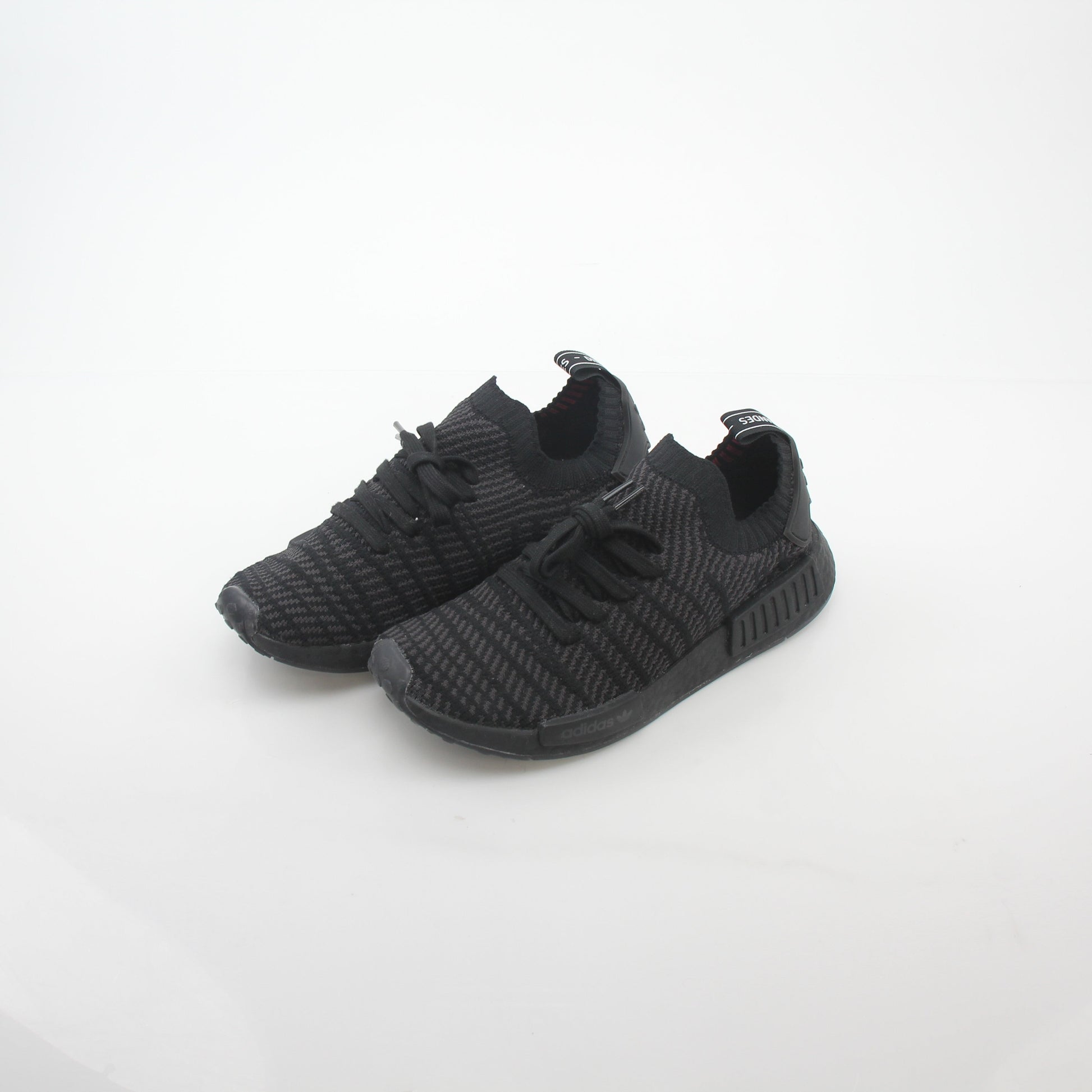 Black Adidas NMD R1 STLT Primeknit sneakers with white Boost sole, featuring sleek design and modern athletic style.