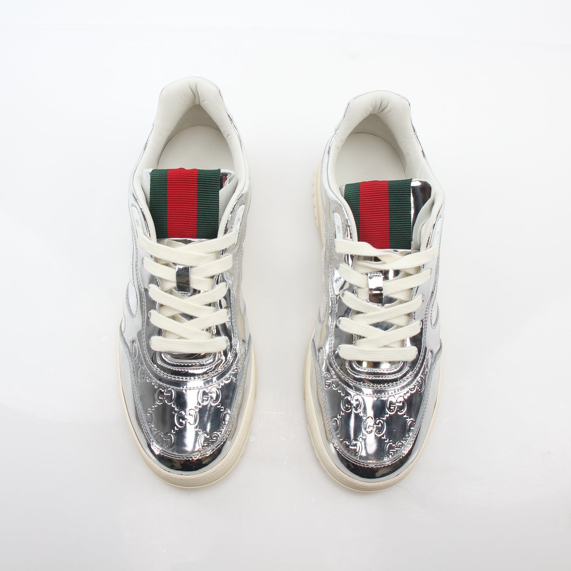 Silver metallic Gucci Re-Web sneakers with white soles and laces, showcasing the stylish logo design.