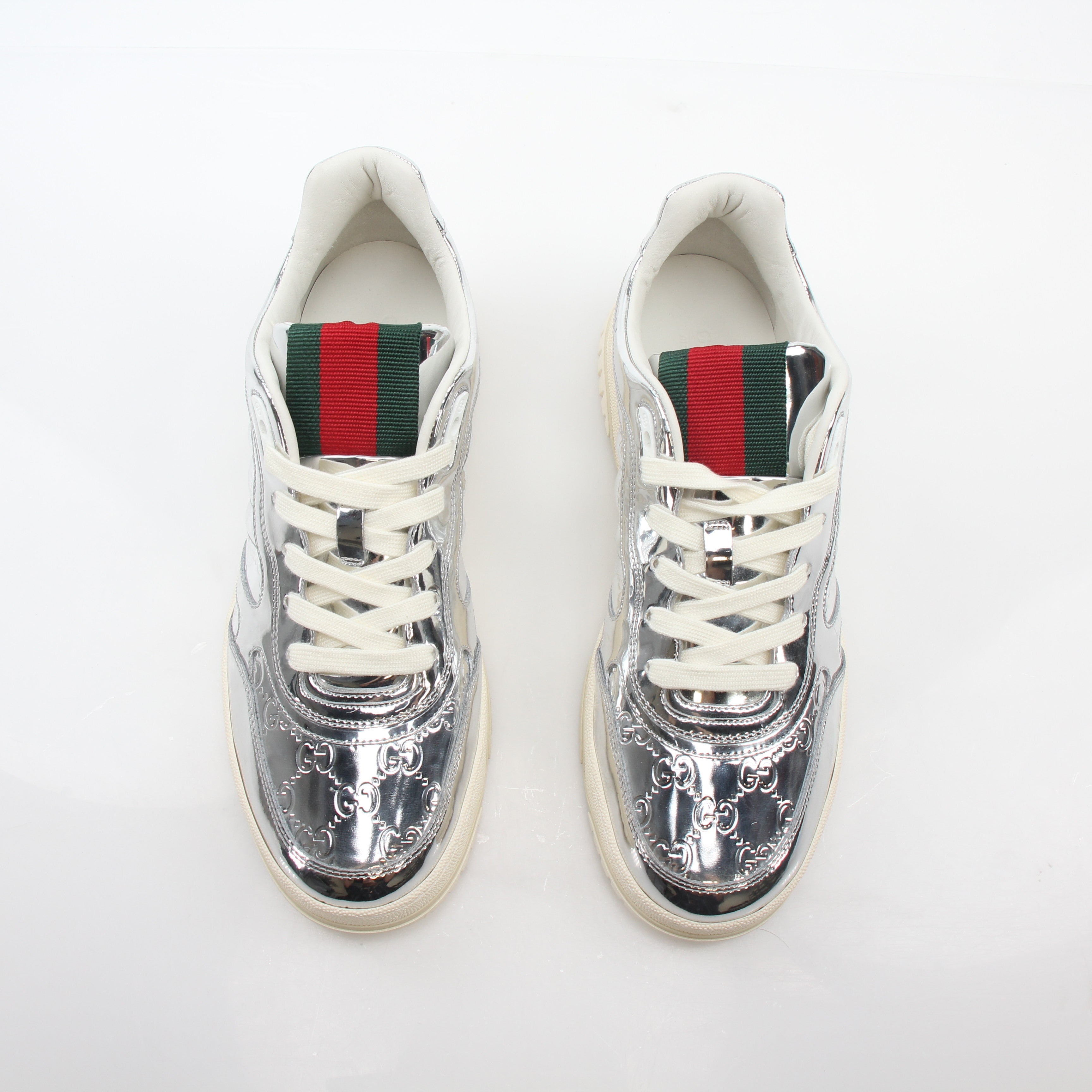 Silver metallic Gucci Re-Web sneakers with white soles and laces, showcasing the stylish logo design.