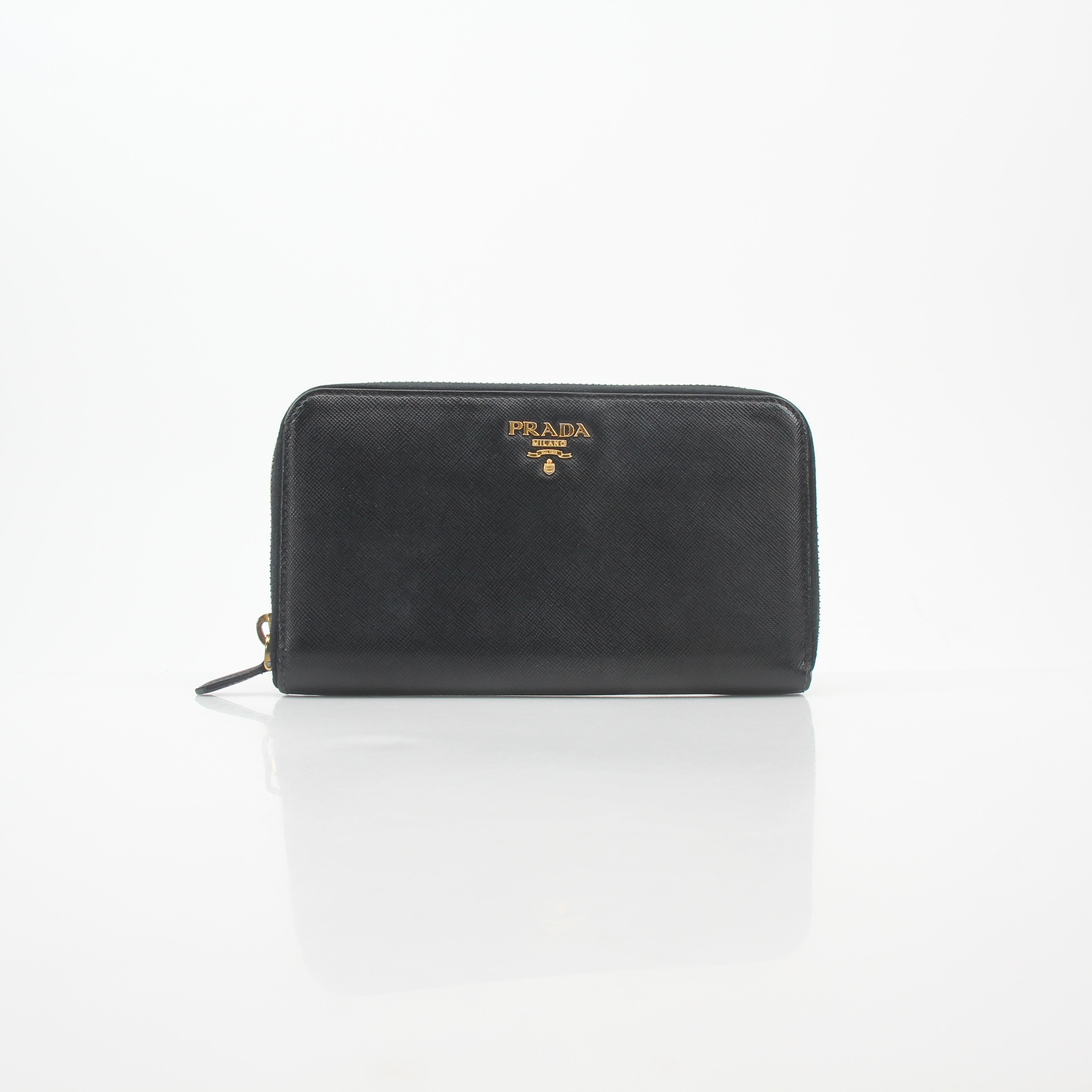 Prada black saffiano leather zip-around wallet with metal logo detail, displayed on a neutral background.