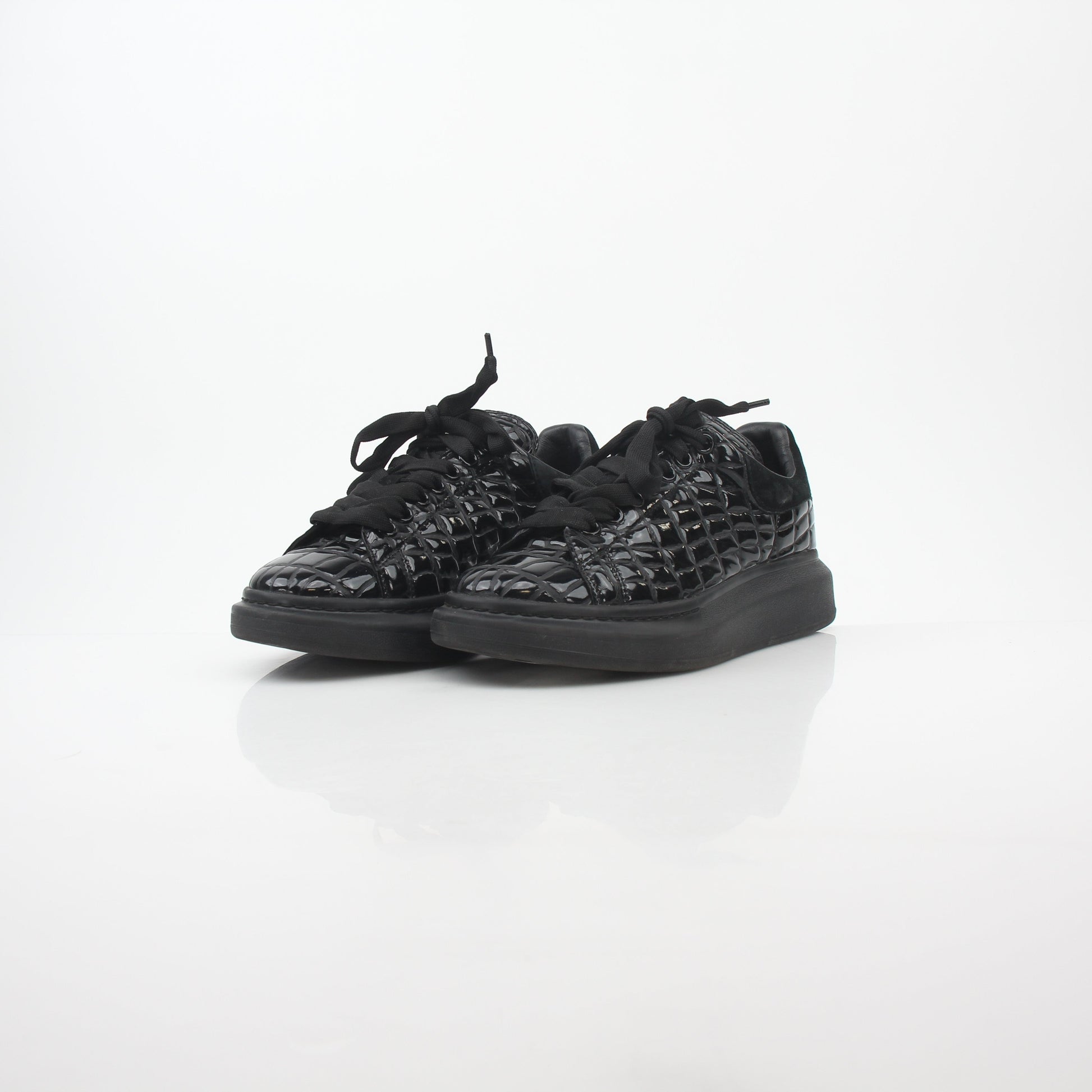Black croc-embossed Alexander McQueen oversized sneakers with chunky soles and branding, displayed on a neutral background.