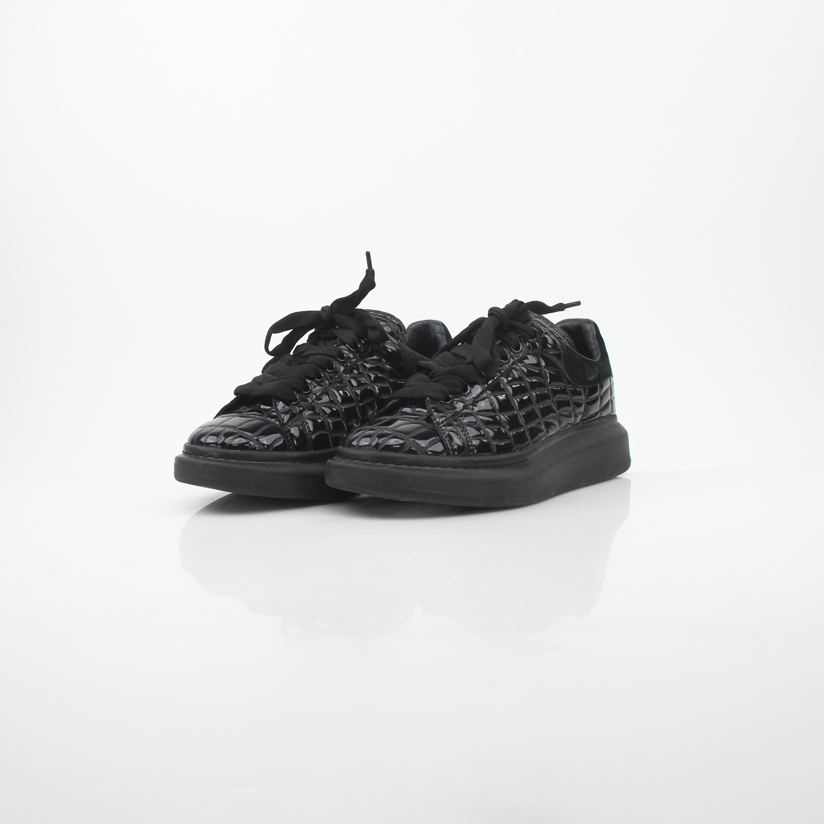 Black croc-embossed Alexander McQueen oversized sneakers with chunky soles and branding, displayed on a neutral background.