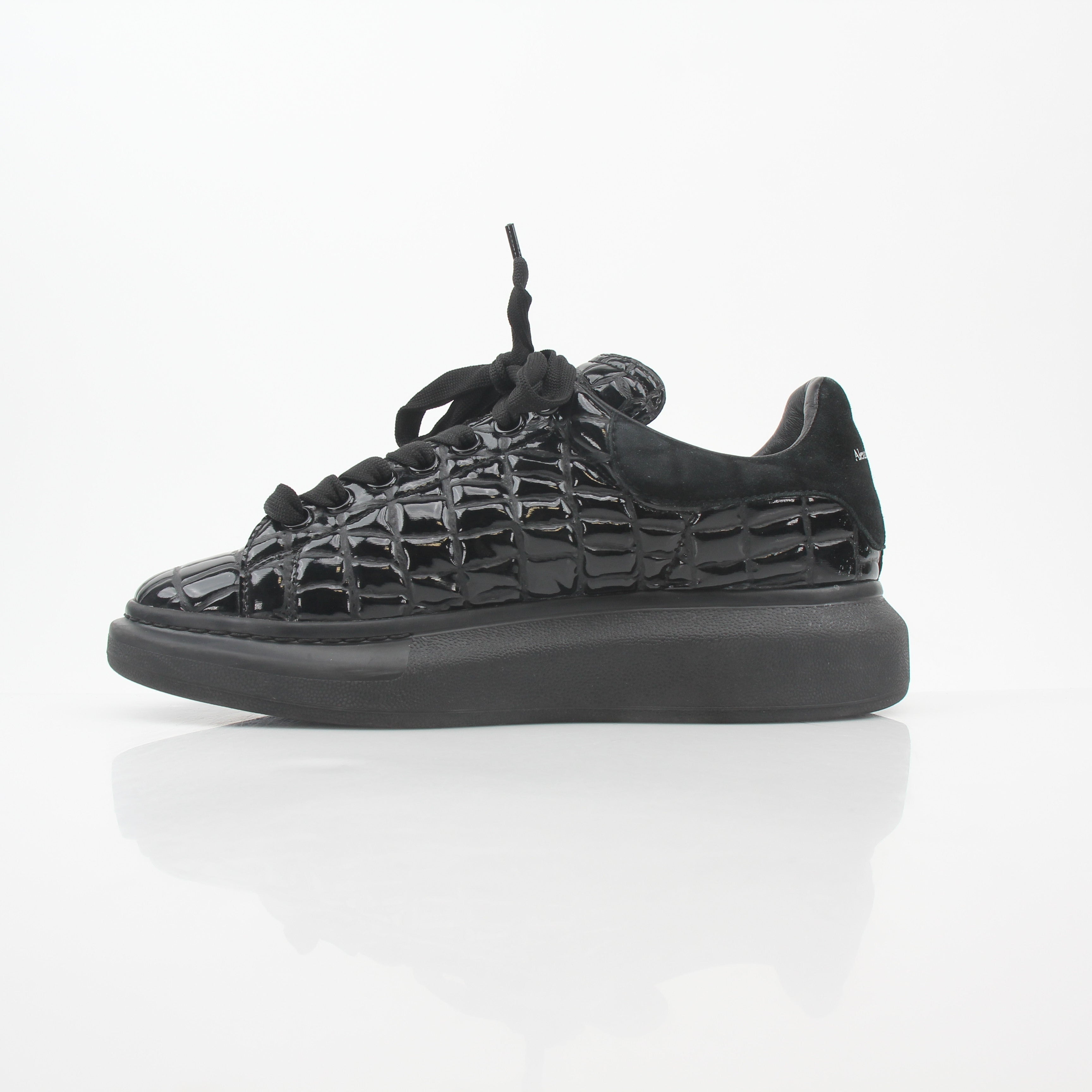 Black croc-embossed Alexander McQueen oversized sneakers with chunky soles and lace-up design, displayed on a neutral background.